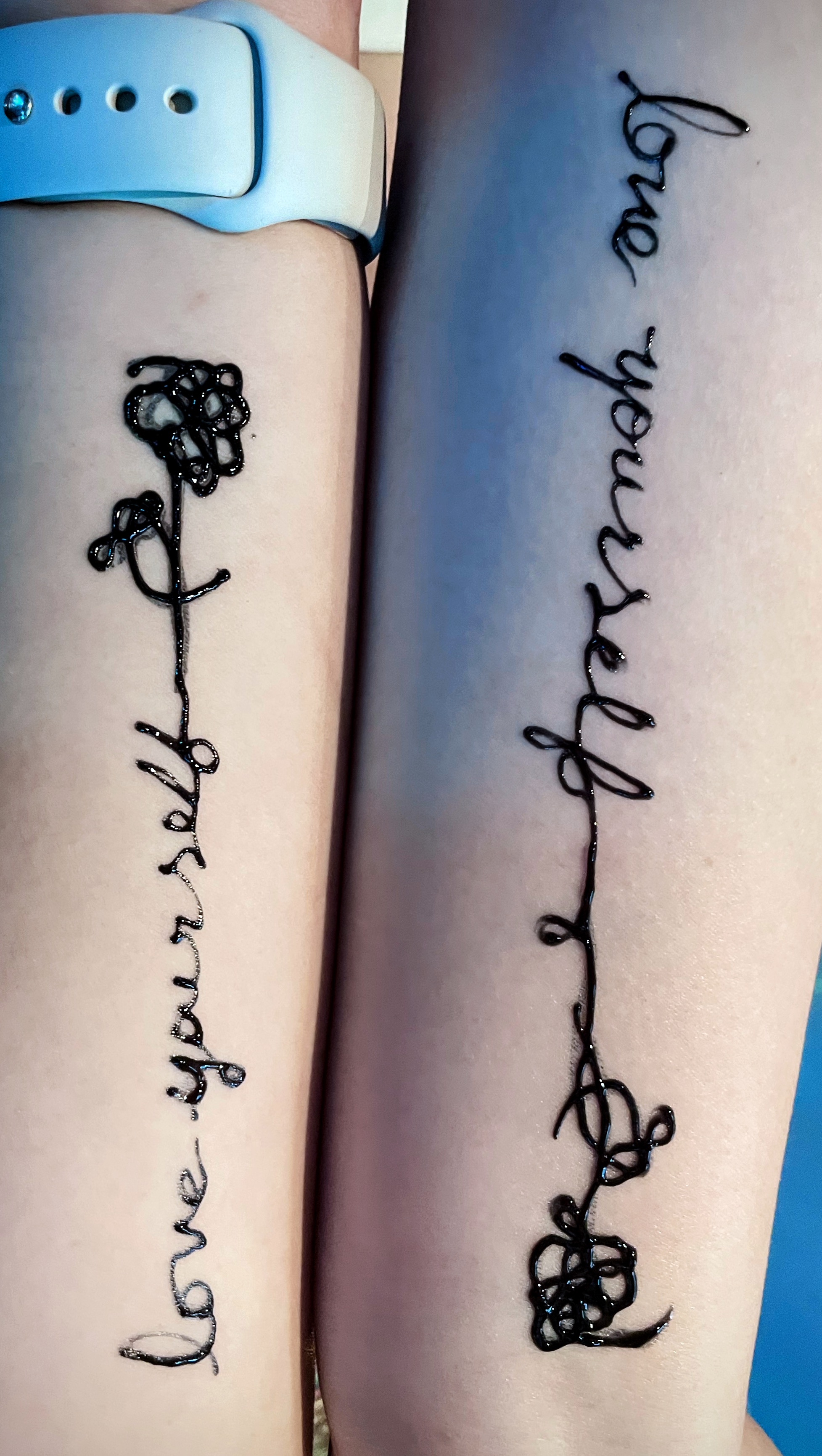 Two girls' arms, who got jagua tattoos that are the same. They say love yourself, with a flower attached at the end.